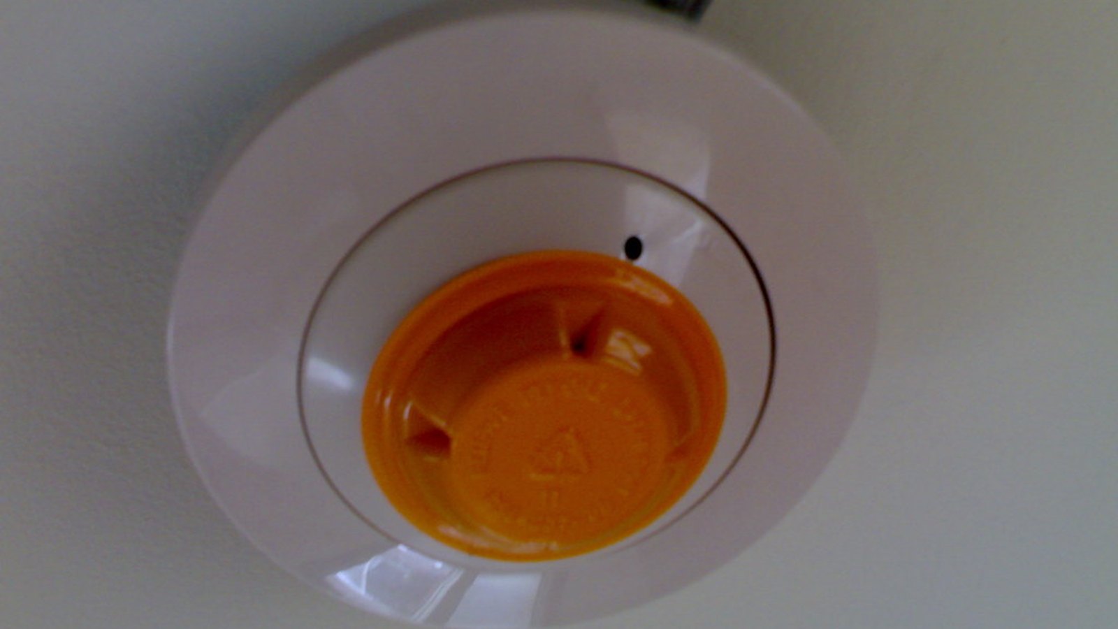 Weißer Rauchmelder mit orangefarbener Kappe an einer Zimmerdecke