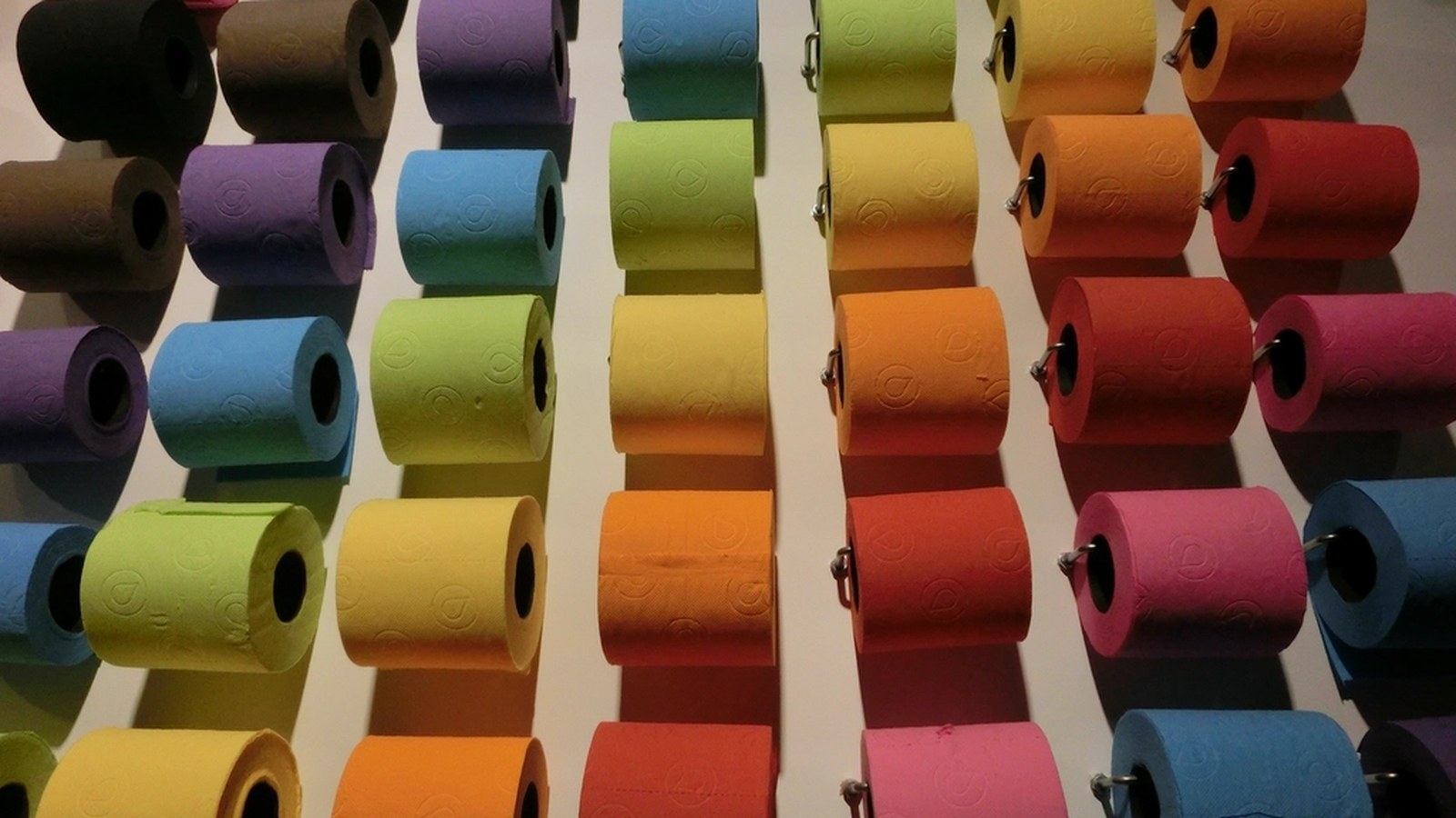 Bunte Toilettenpapierrollen in Reihen an einer Wand